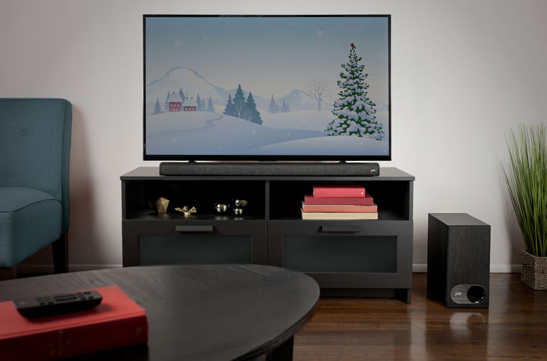 A room with a TV and sound bar sitting on a TV stand. A subwoofer is on the floor next to them.