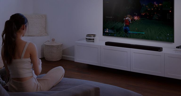 a couple watching TV with a large sound bar sitting under it.