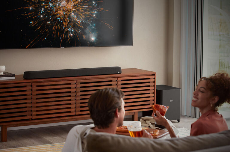 A couple eating pizza and watching TV.