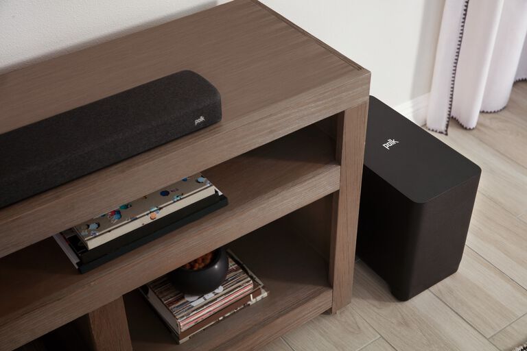 A soundbar on a table with a subwoofer on the ground next to it.