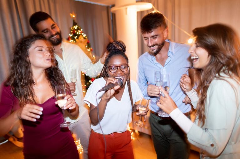 A woman singing into a microphone with friends laughing and singing with her. A woman singing into a microphone with friends laughing and singing with her.