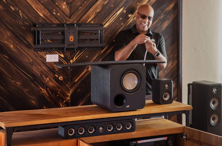 A soundbar on a table with a subwoofer on the ground next to it. A soundbar on a table with a subwoofer on the ground next to it.