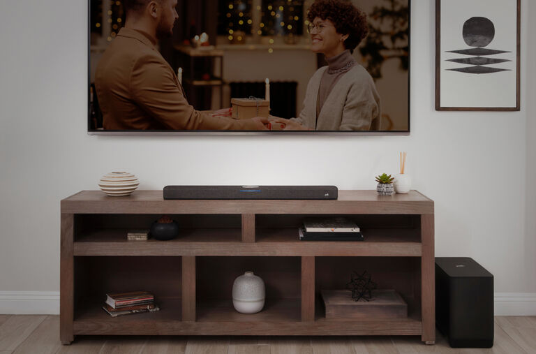 A mounted TV with a soundbar on the table below, and a subwoofer on the floor beside the table.